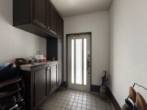 市原市下野の中古戸建ての玄関スペース。タイル張りの床に、収納力の高いダークブラウンのシューズボックスが設置されている。