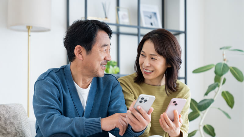 夫婦でスマホを見て寛ぐ様子の画像