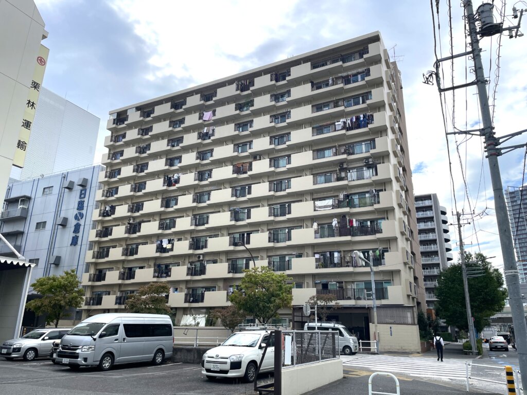 マリンシティダイヤモンドパレスのバルコニー側の外観写真。多くの住戸で洗濯物が干されており、生活感がうかがえる。手前には駐車場があり、隣接する建物も写っている。