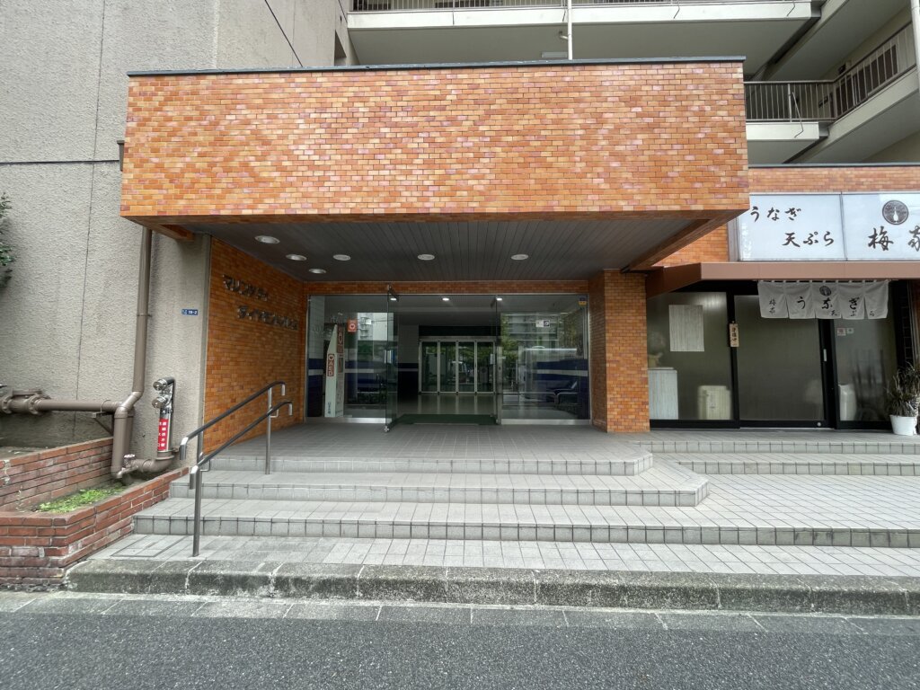 レンガ調のタイル貼りが特徴的なマリンシティダイヤモンドパレスのメインエントランス。階段とスロープが併設されており、ガラスの自動ドアから館内に入れる。右隣にはテナントのうなぎ屋がある。