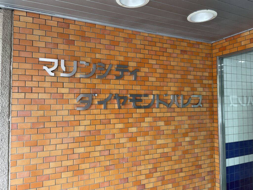 マリンシティダイヤモンドパレスのエントランス脇のレンガ壁に設置された館銘板。「マリンシティダイヤモンドパレス」という銀色の切り文字がはっきりと写っている。