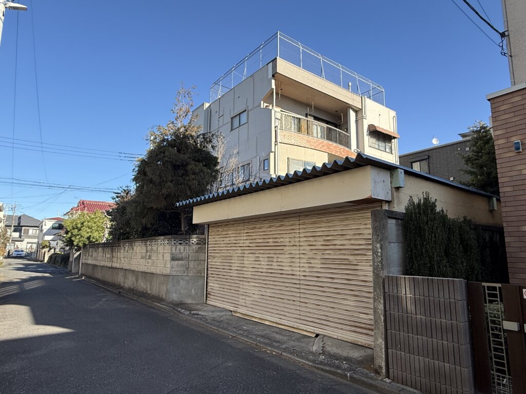 南区別所2丁目売地の敷地外観の別アングル。既存のシャッター付きガレージ部分などが写っている。