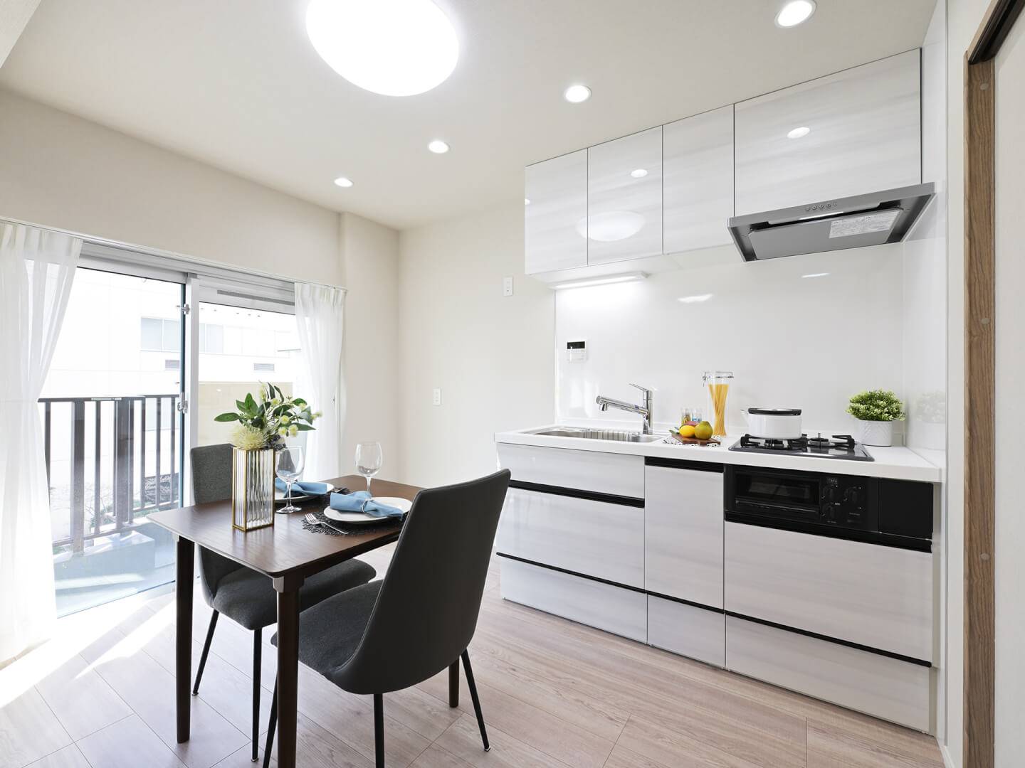白を基調としたシステムキッチンと、その手前に配置されたダイニングテーブル。キッチンは収納豊富で、壁面パネルはお手入れがしやすい素材が使われている。