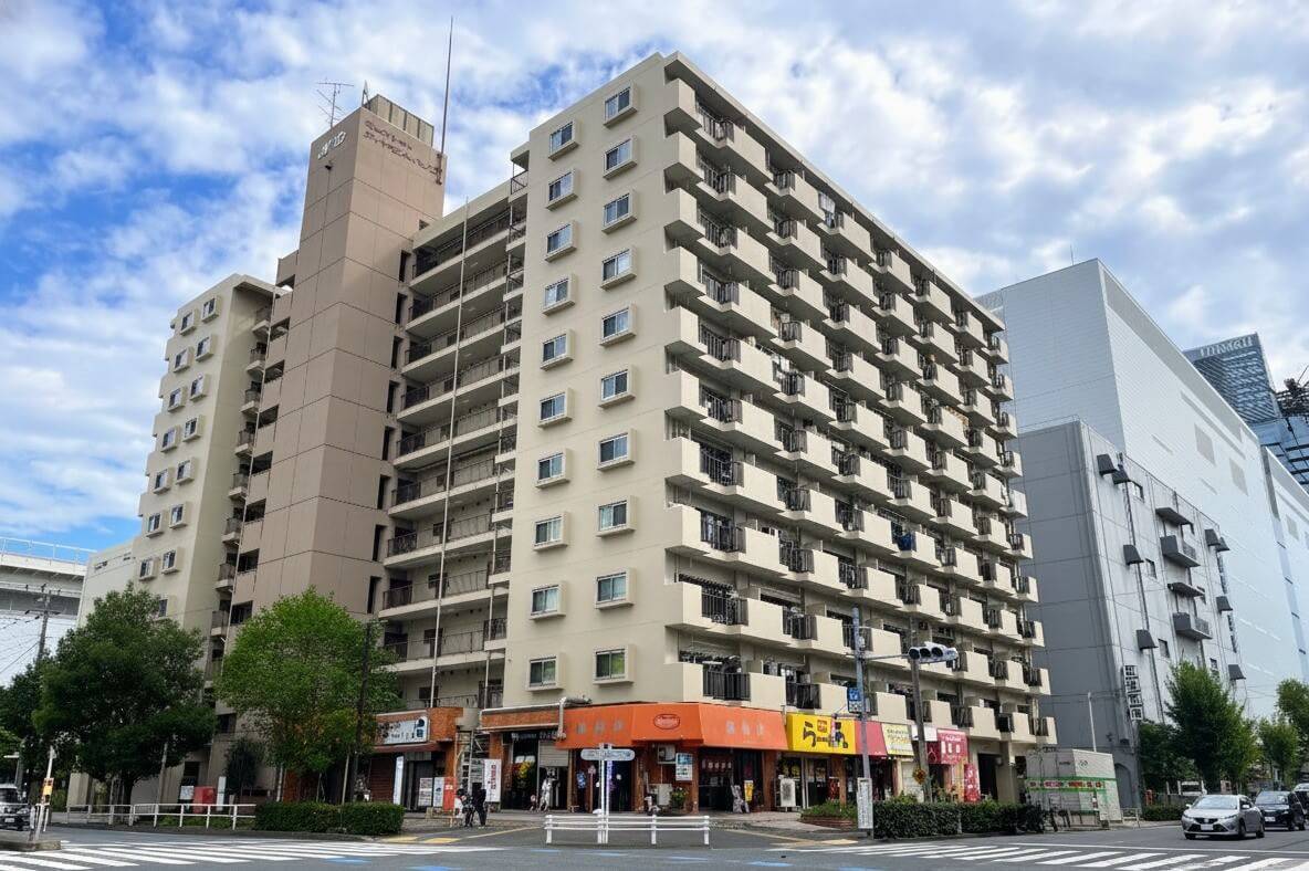 青空の下に建つ11階建てマンション「マリンシティダイヤモンドパレス」の外観。1階店舗部分と周辺の道路状況