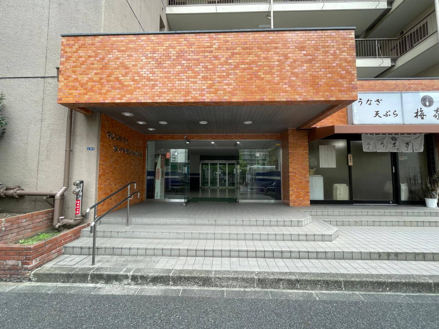 レンガ調のタイル貼りが特徴的なマリンシティダイヤモンドパレスのメインエントランス。階段とスロープが併設されており、ガラスの自動ドアから館内に入れる。右隣にはテナントのうなぎ屋がある。