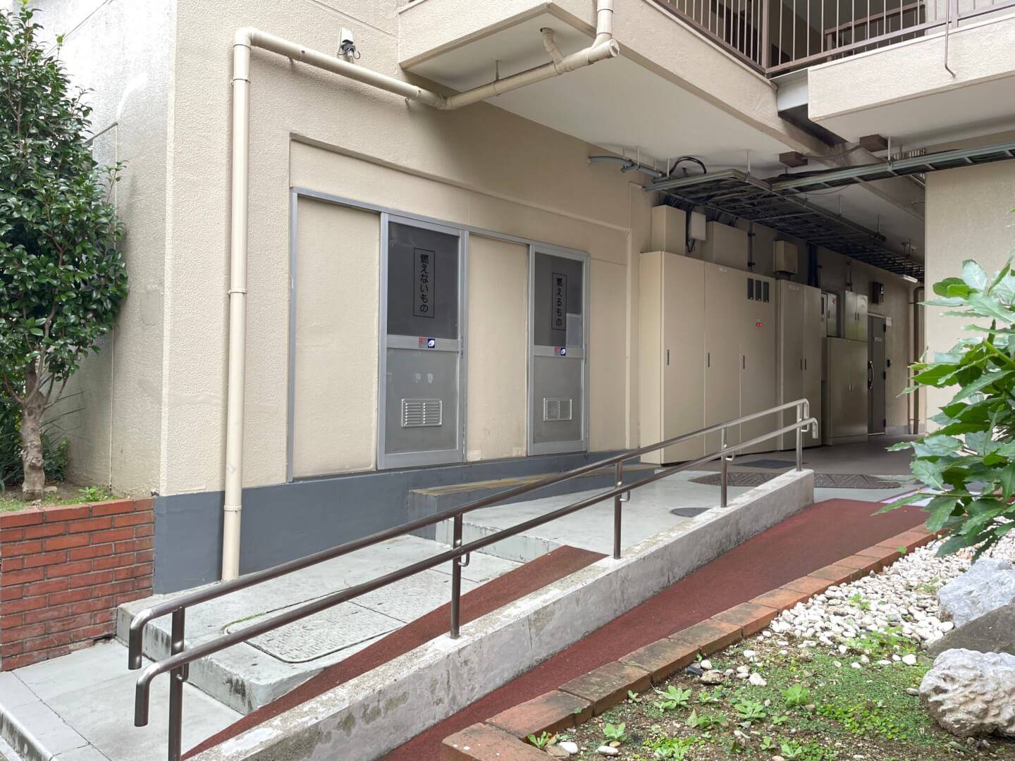 マリンシティダイヤモンドパレス敷地内のスロープとゴミ置き場。手すり付きの緩やかなスロープがあり、その奥に「燃えないもの」などの表示があるゴミ収集スペースが設置されている。