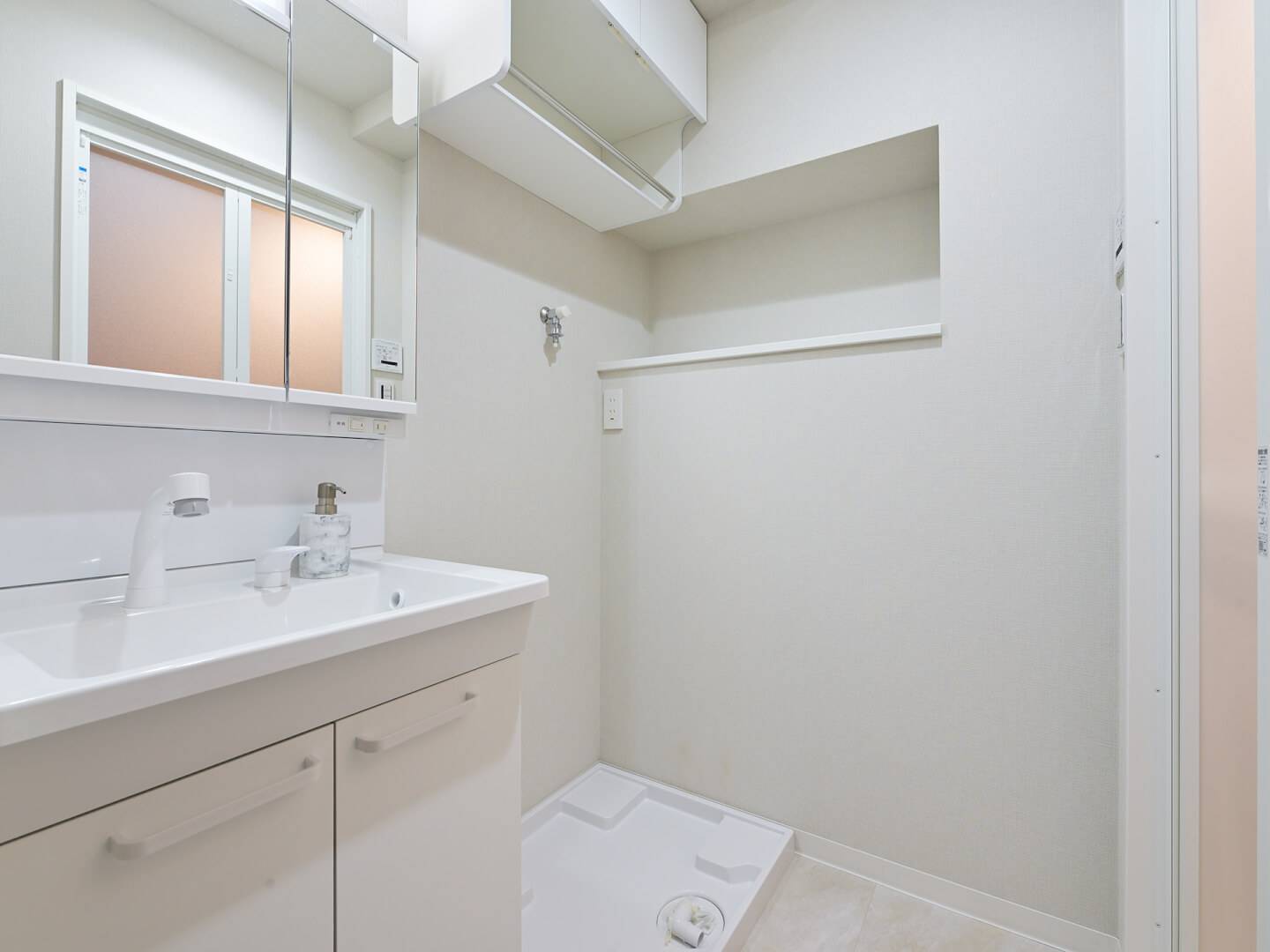 白を基調とした清潔感のある洗面脱衣室。収納力のある三面鏡付き洗面台と、上部に棚が設けられた洗濯機置き場スペース。
